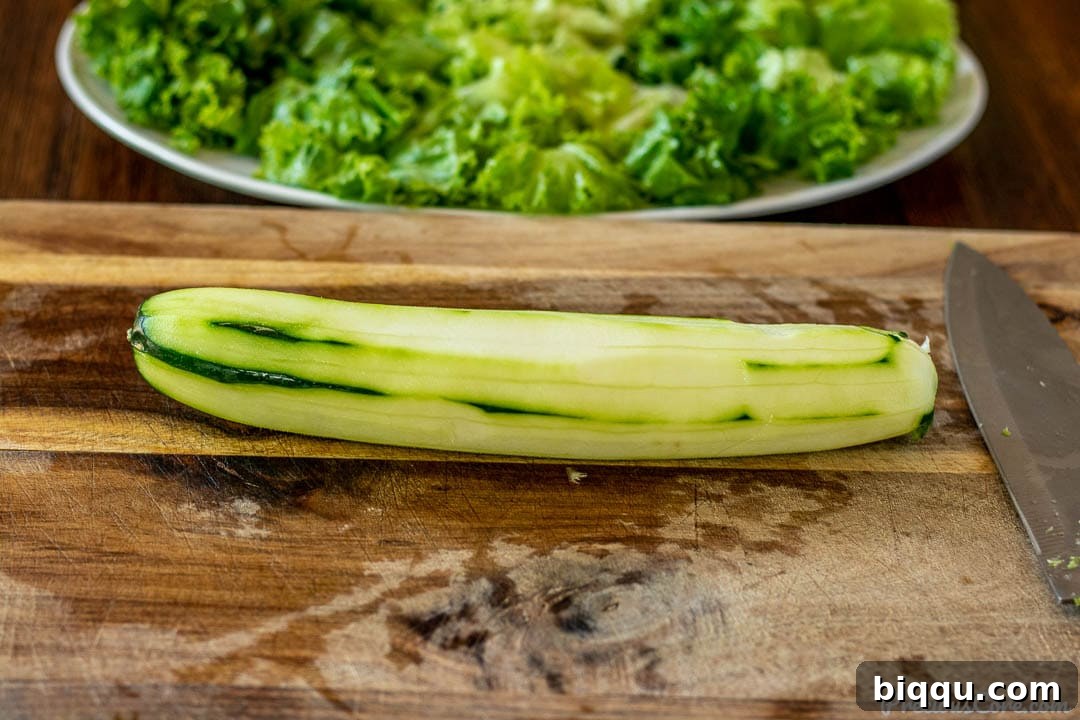 A freshly peeled garden cucumber resting on a wooden chopping board, ready for slicing.