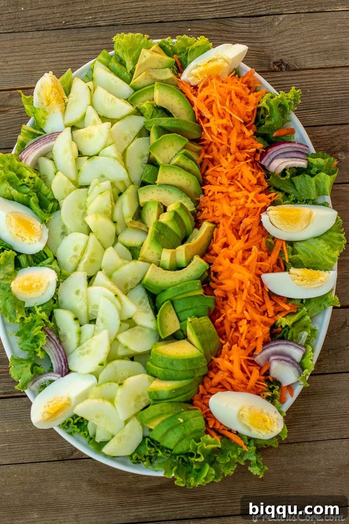 A vibrant arrangement of all the fresh vegetables for lettuce salad on a pristine white serving platter, showcasing the colorful ingredients.