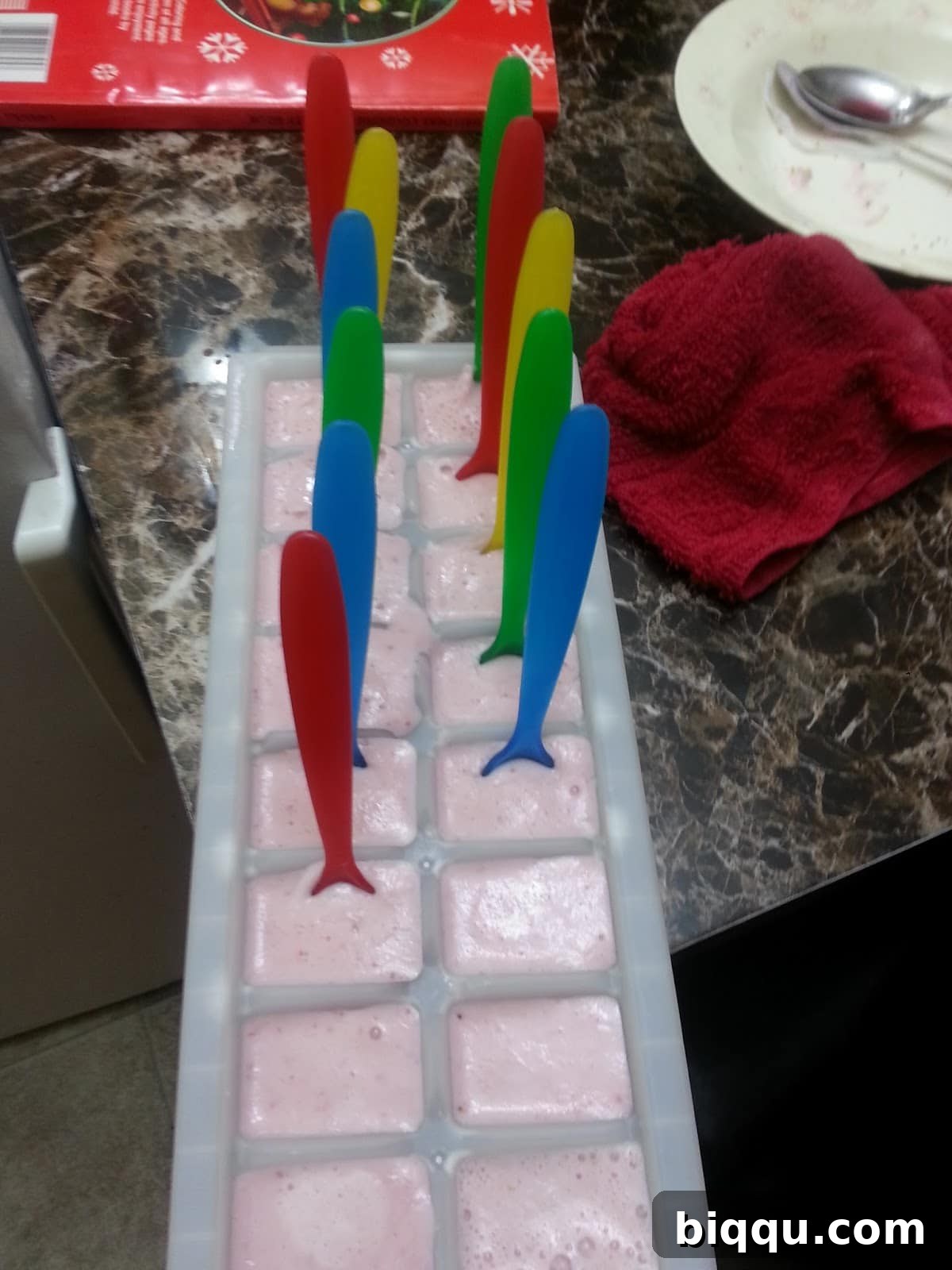 Popsicle sticks inserted into partially frozen strawberry yogurt popsicles in trays