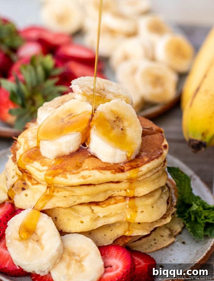 Stack of golden banana pancakes with sliced bananas and maple syrup drizzling on top