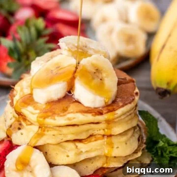 Stack of golden banana pancakes with sliced bananas and maple syrup drizzling on top