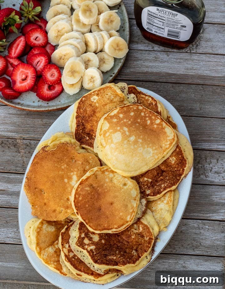 Platter of fluffy banana pancakes with fresh sliced bananas and strawberries on the side