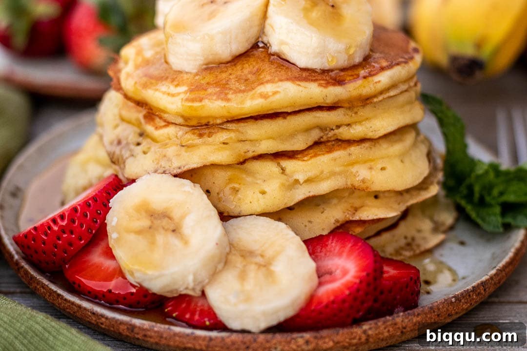 Close-up of fluffy banana pancakes on a plate, adorned with sliced bananas and strawberries