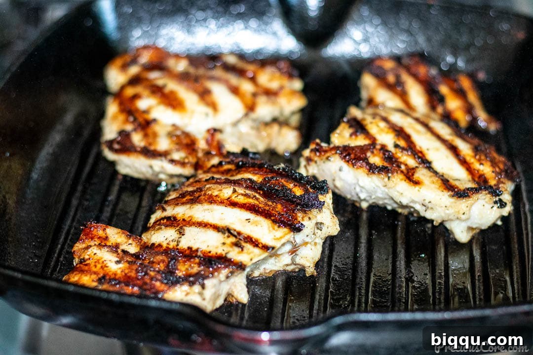 Succulent Grilled Boneless Chicken Thighs 5 Chicken thighs sizzling on an indoor grill pan, showing early char marks