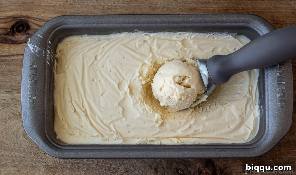 Close-up of freshly made homemade vanilla ice cream chilling in a loaf pan, covered with plastic wrap.