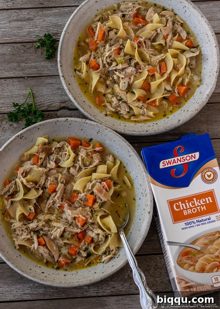 Two bowls of quick chicken noodle soup, with a carton of Swanson Chicken Broth placed next to them, emphasizing the broth as a key ingredient