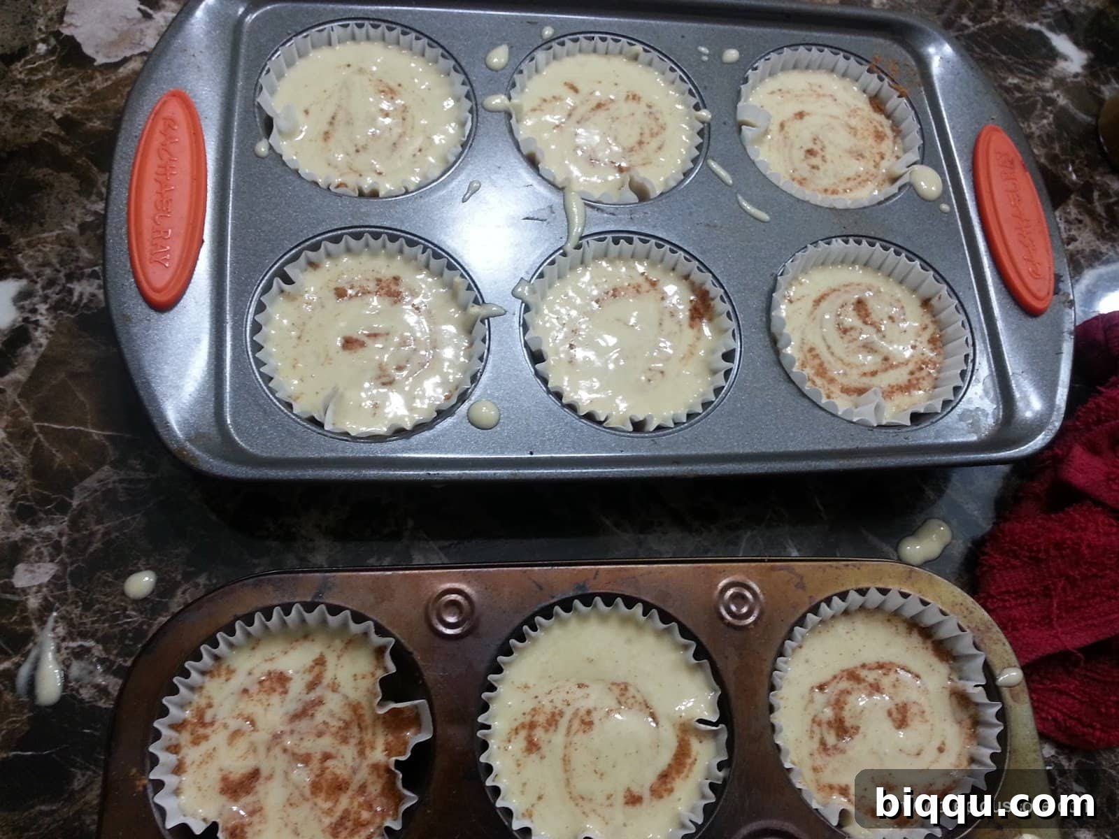 Muffin pan full of banana cake batter swirled with cinnamon.