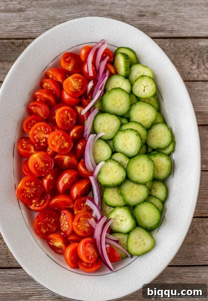 Close-up of freshly chopped cucumbers, tomatoes, and thinly sliced red onions artfully arranged on a serving platter.