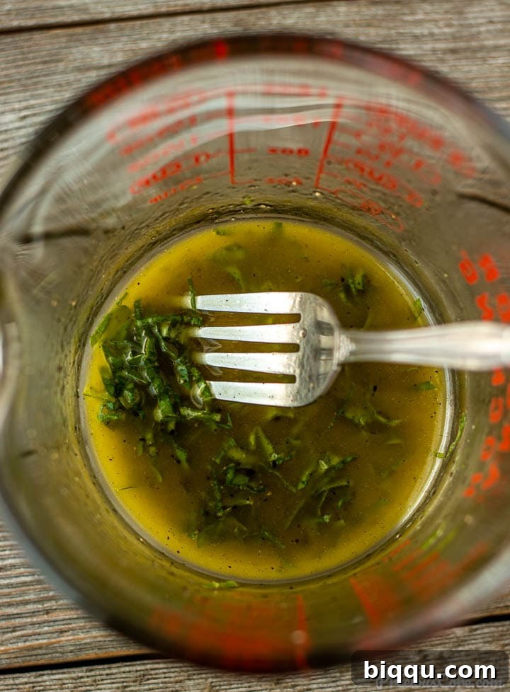 Freshly prepared lemon basil salad dressing in a clear measuring cup, showing its vibrant green specks.