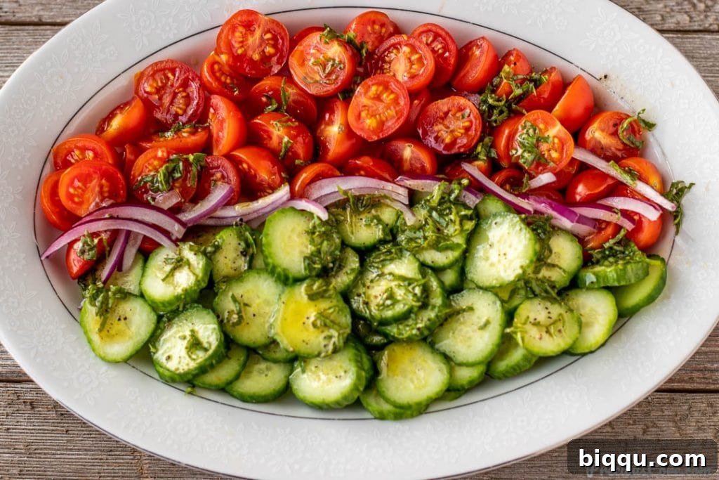 Prepared tomato cucumber salad with the vibrant basil lemon dressing generously drizzled over the top, ready for tossing.