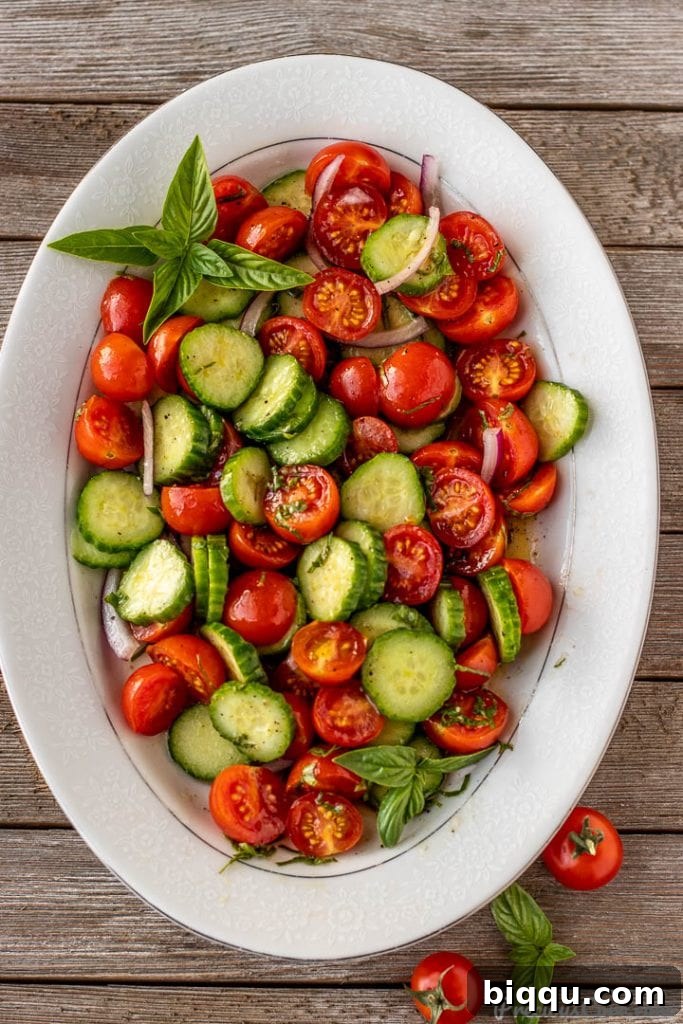 A large bowl of cucumber tomato onion salad, freshly tossed with dressing, ready to be served.