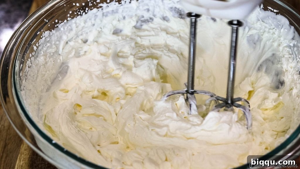 Whipping cold heavy cream in a bowl until it forms stiff, stable peaks