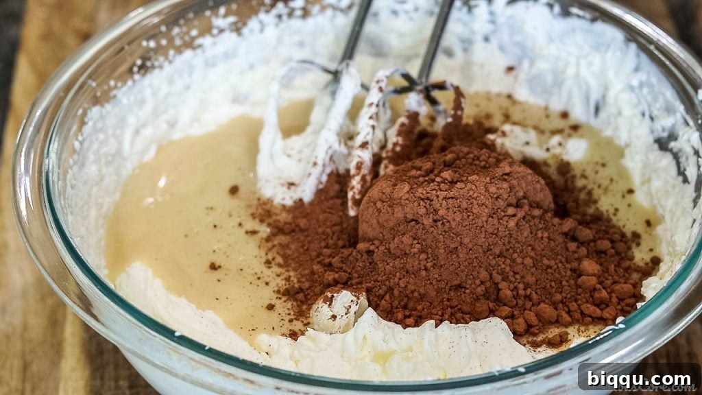 Sweetened condensed milk and cocoa powder being added to the bowl of whipped cream