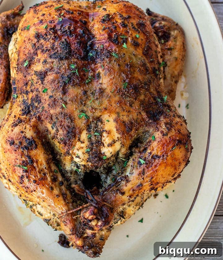 Whole herb roasted chicken on a platter, garnished with fresh herbs