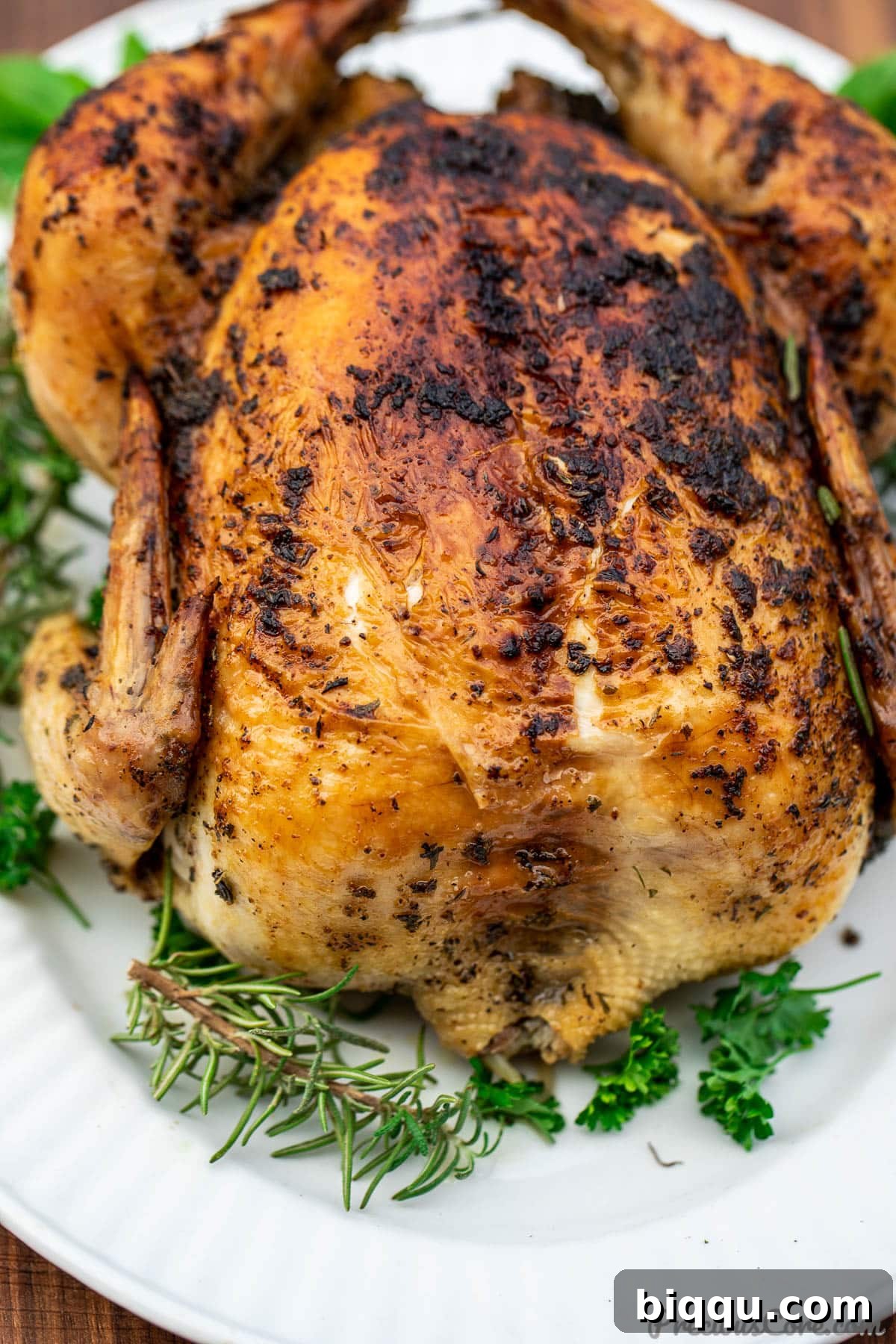 Whole herb roasted chicken on a platter, elegantly garnished with fresh sprigs of herbs like rosemary and thyme.