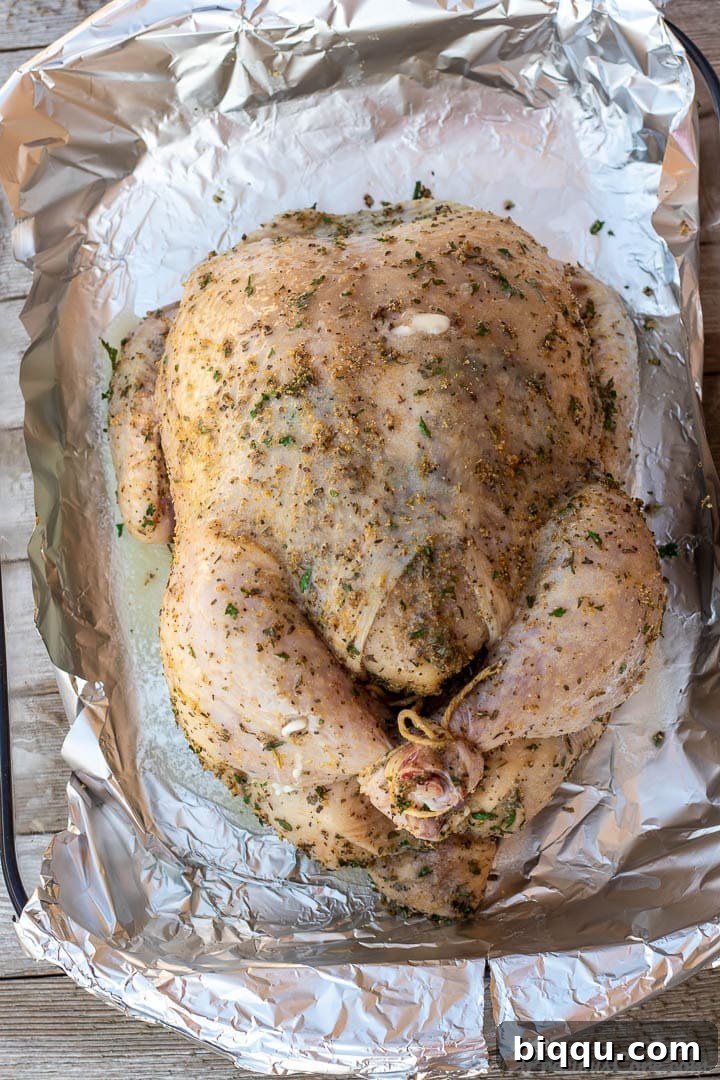 A whole chicken, seasoned with herbs and spices, resting in a baking dish before roasting.