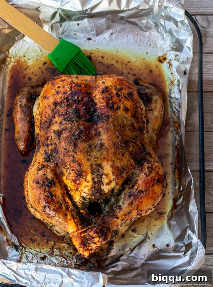 A golden brown roast chicken, glistening with pan juices, resting in its baking dish after being perfectly cooked.