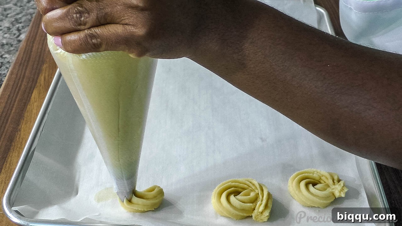 A hand expertly piping butter cookie dough onto a parchment-lined baking sheet, forming delicate swirls.
