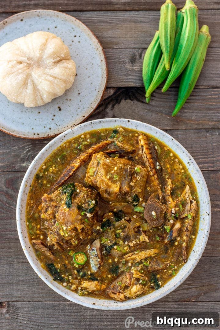 A bowl of vibrant African Okra Soup, garnished with fresh ingredients, served alongside a plate of fluffy Garri fufu