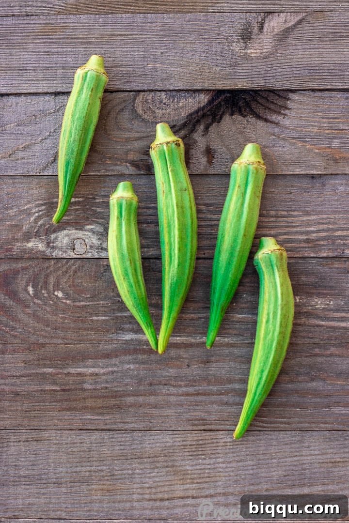 Fresh, vibrant green okra pods arranged artfully on a rustic wooden board, ready for preparation.
