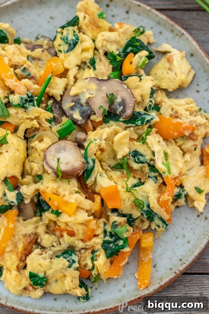 Closer shot of fluffy scrambled eggs with visible pieces of mushroom, bell pepper, and spinach