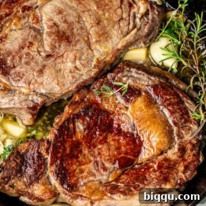 Two ribeye steaks in a cast iron skillet with rosemary, thyme, and garlic.