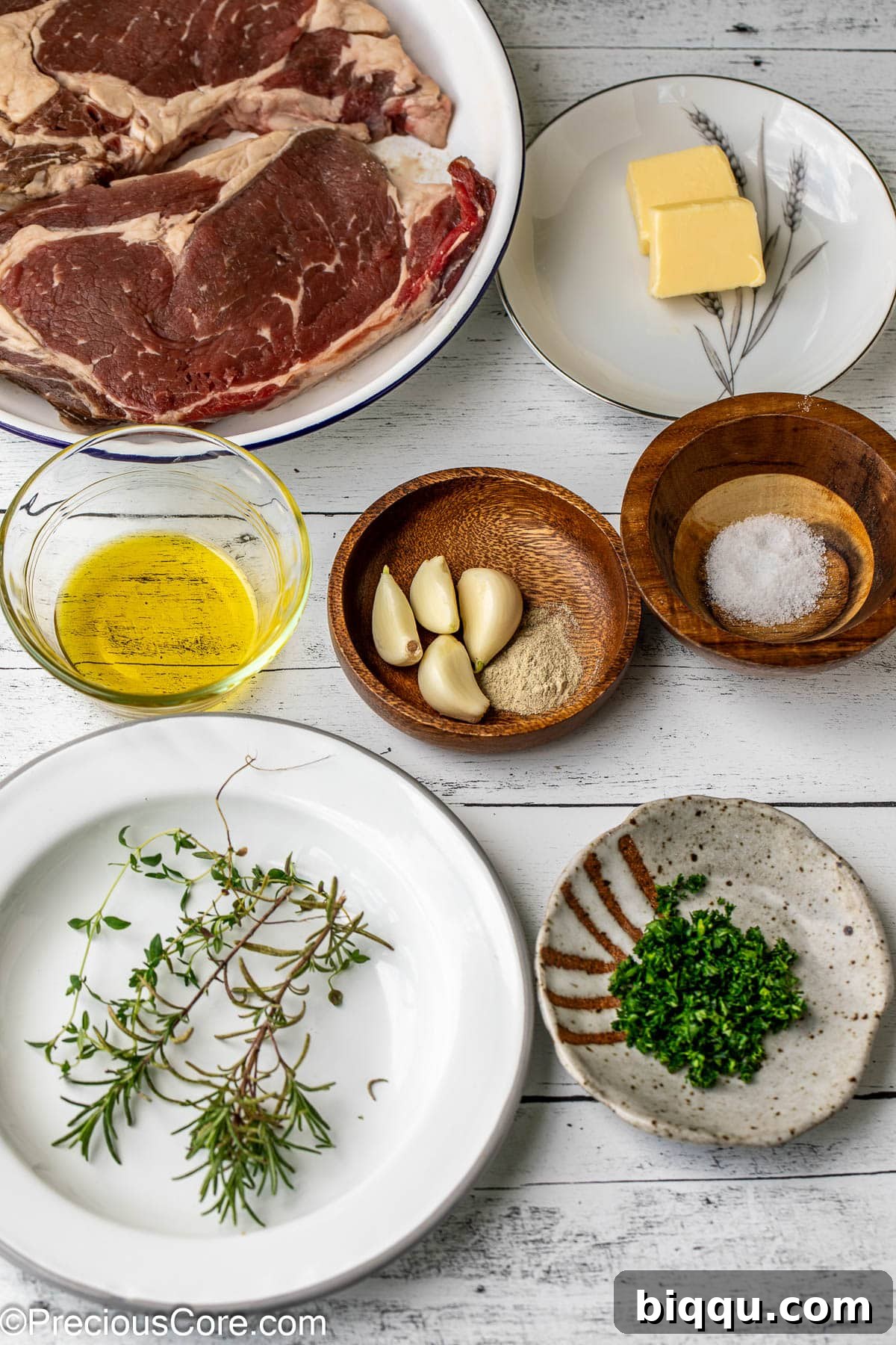 Seared Ribeye Perfection 4 A selection of fresh ingredients including ribeye steaks, olive oil, salt, pepper, garlic, rosemary, thyme, and butter, laid out for pan searing.