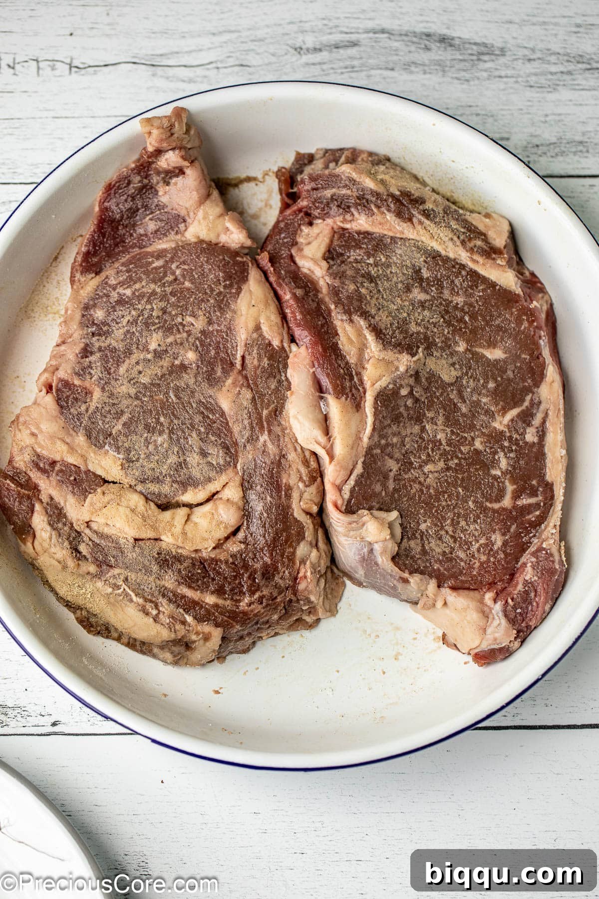 Seared Ribeye Perfection 5 Two seasoned ribeye steaks resting in a white bowl, ready for pan searing.