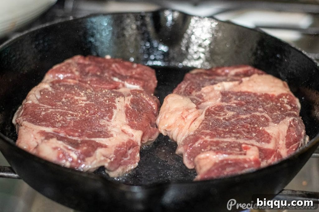 Seared Ribeye Perfection 6 A raw ribeye steak sizzling as it's placed into a hot cast iron skillet, beginning to sear.
