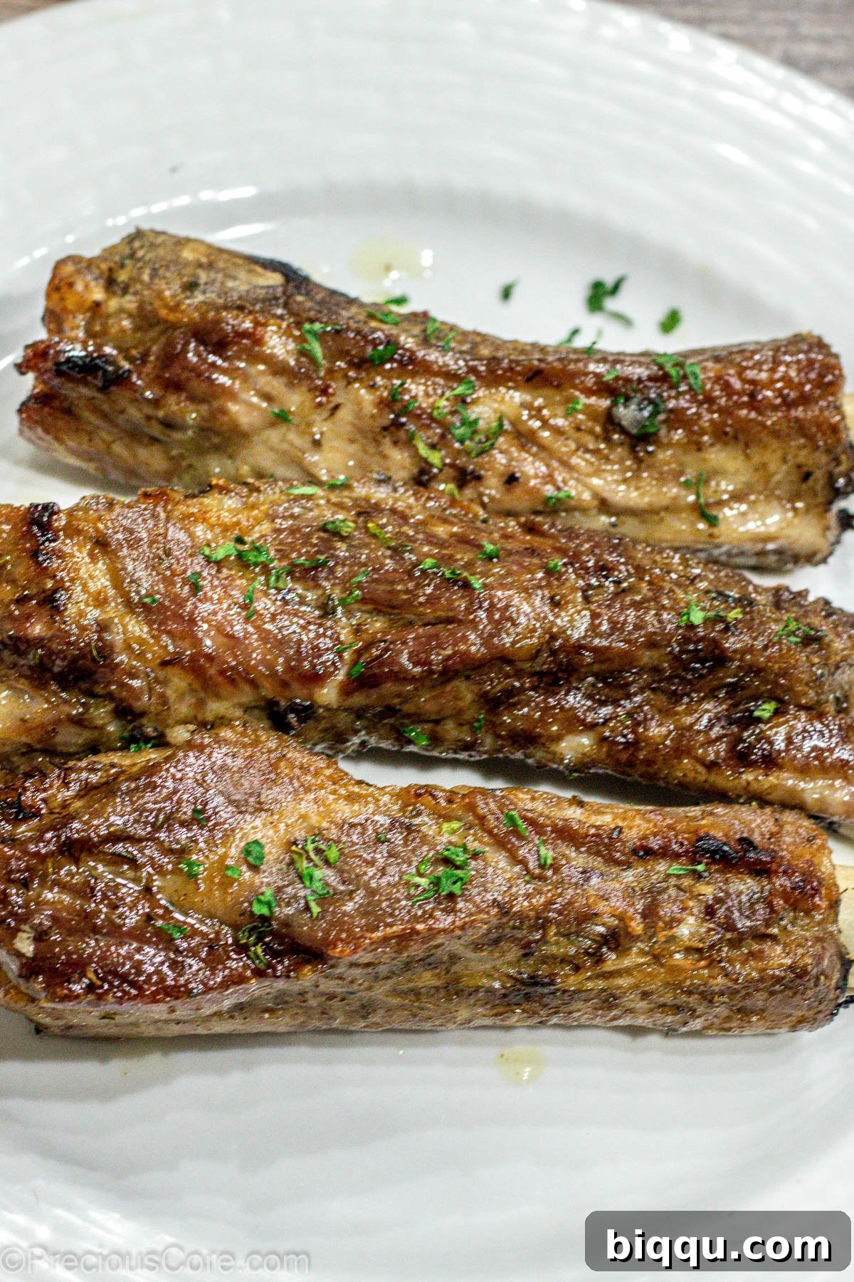 Three perfectly baked ribs resting on a pristine white plate, garnished subtly.