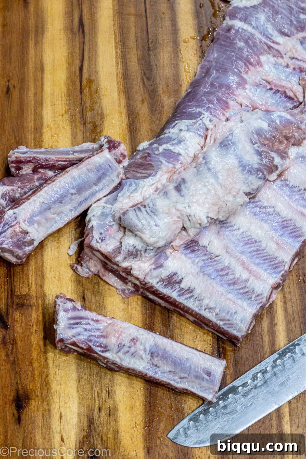 Several portions of raw spare ribs neatly cut from a rack, laid out on a cutting board, ready for seasoning.