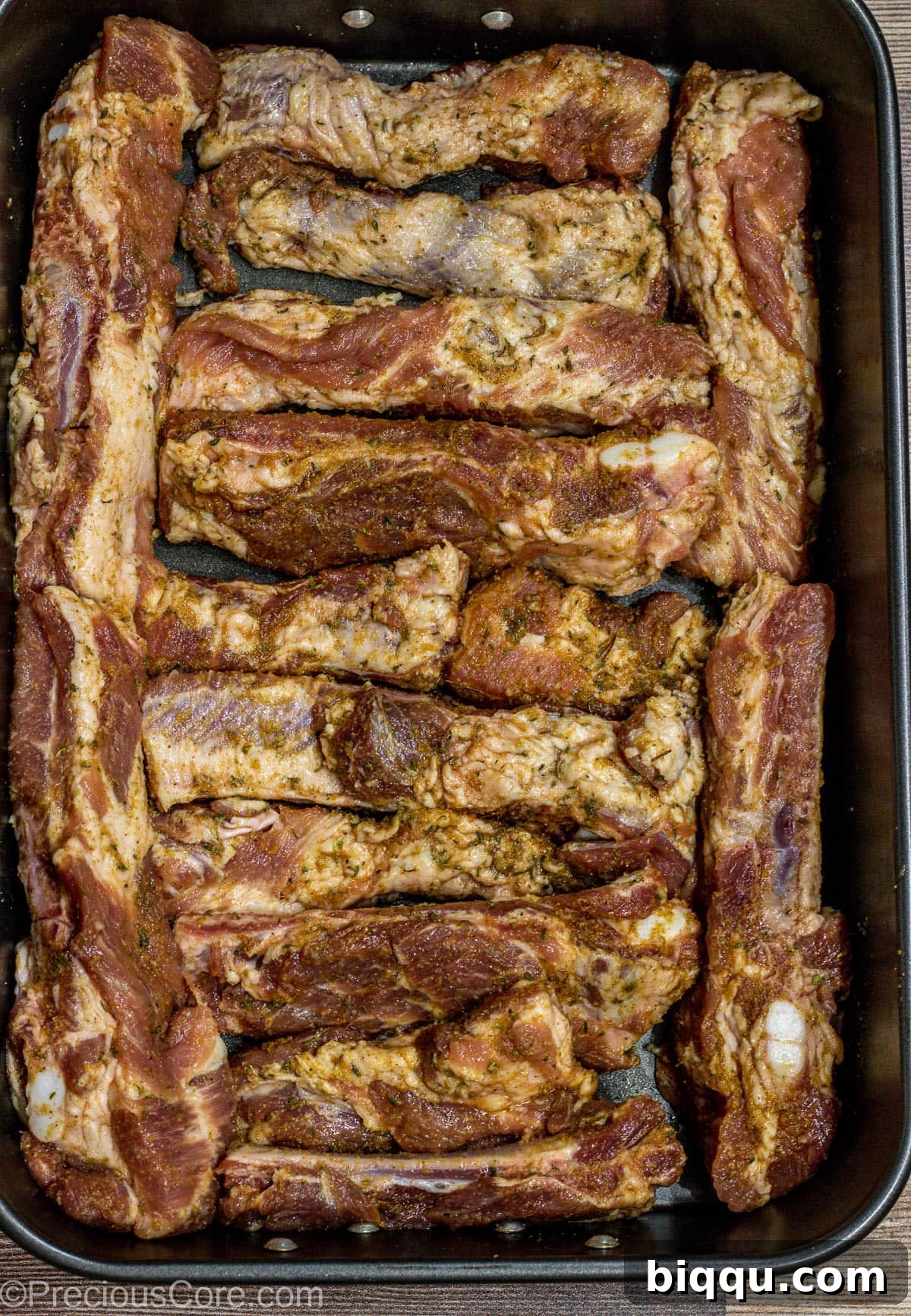 Individual seasoned ribs arranged neatly in a baking dish, coated in a rich dry rub and ready for the oven.