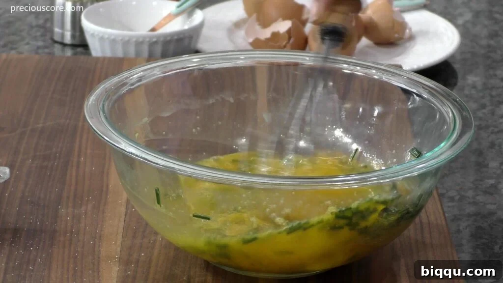 A creamy, yellow egg mixture with visible flecks of green chives, prepared in a bowl and ready for the frittata.