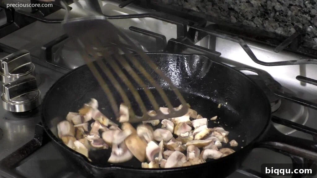 Sliced mushrooms actively sautéing in a hot skillet with oil, showing their softening texture.