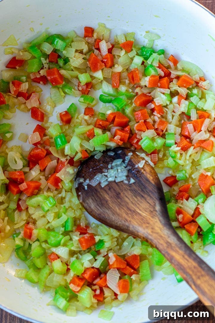 A pot on the stove with a mixture of sautéed onions, garlic, carrots, and celery, forming the aromatic base of the stew.