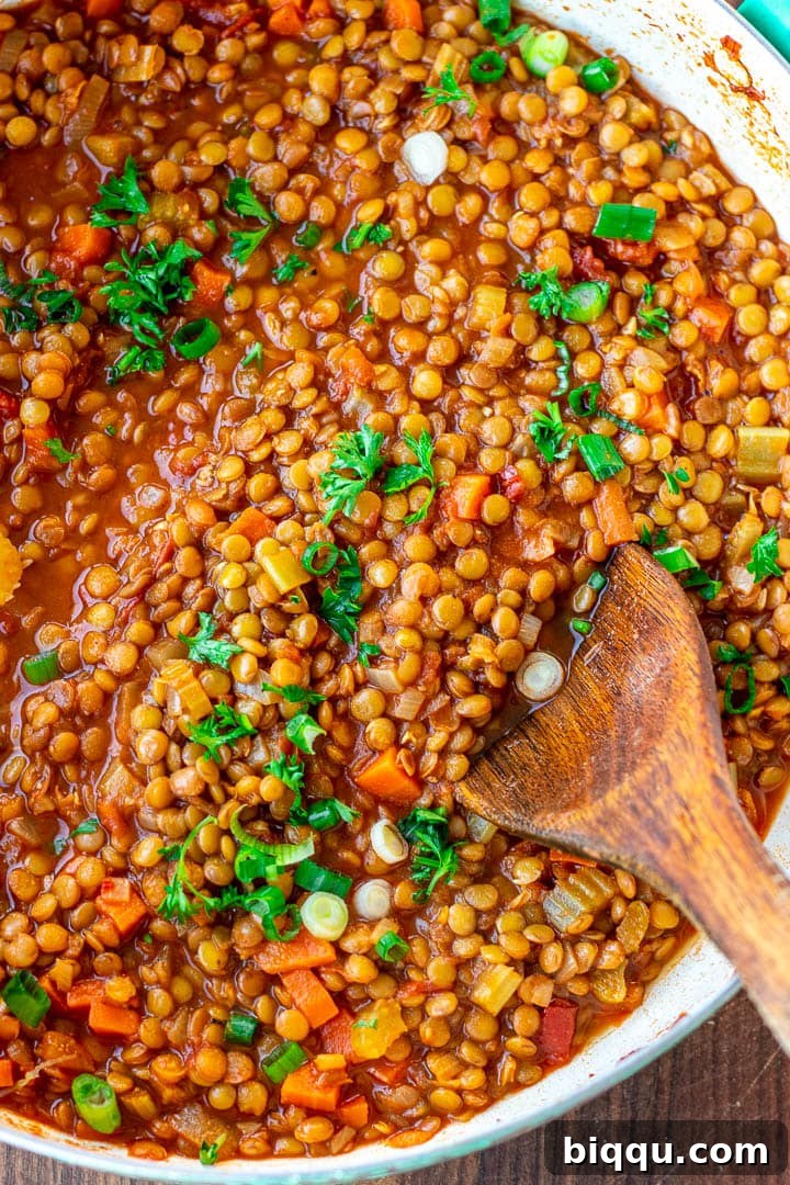 A large pot of Lentil Stew beautifully garnished with chopped fresh parsley and vibrant green onions, ready to be served.