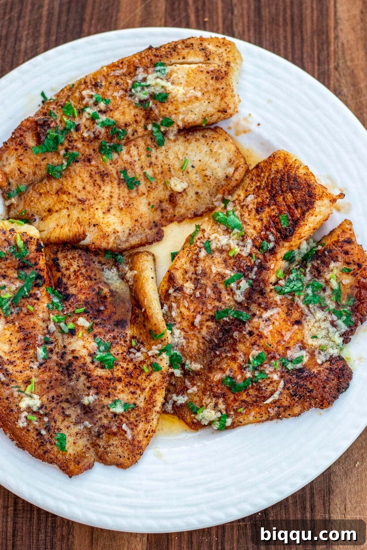 Lemon butter tilapia fillets on a white plate, garnished with fresh parsley and lemon slices, ready to be served.