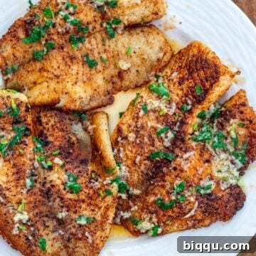 Lemon butter tilapia fillets on a plate, garnished with fresh parsley.