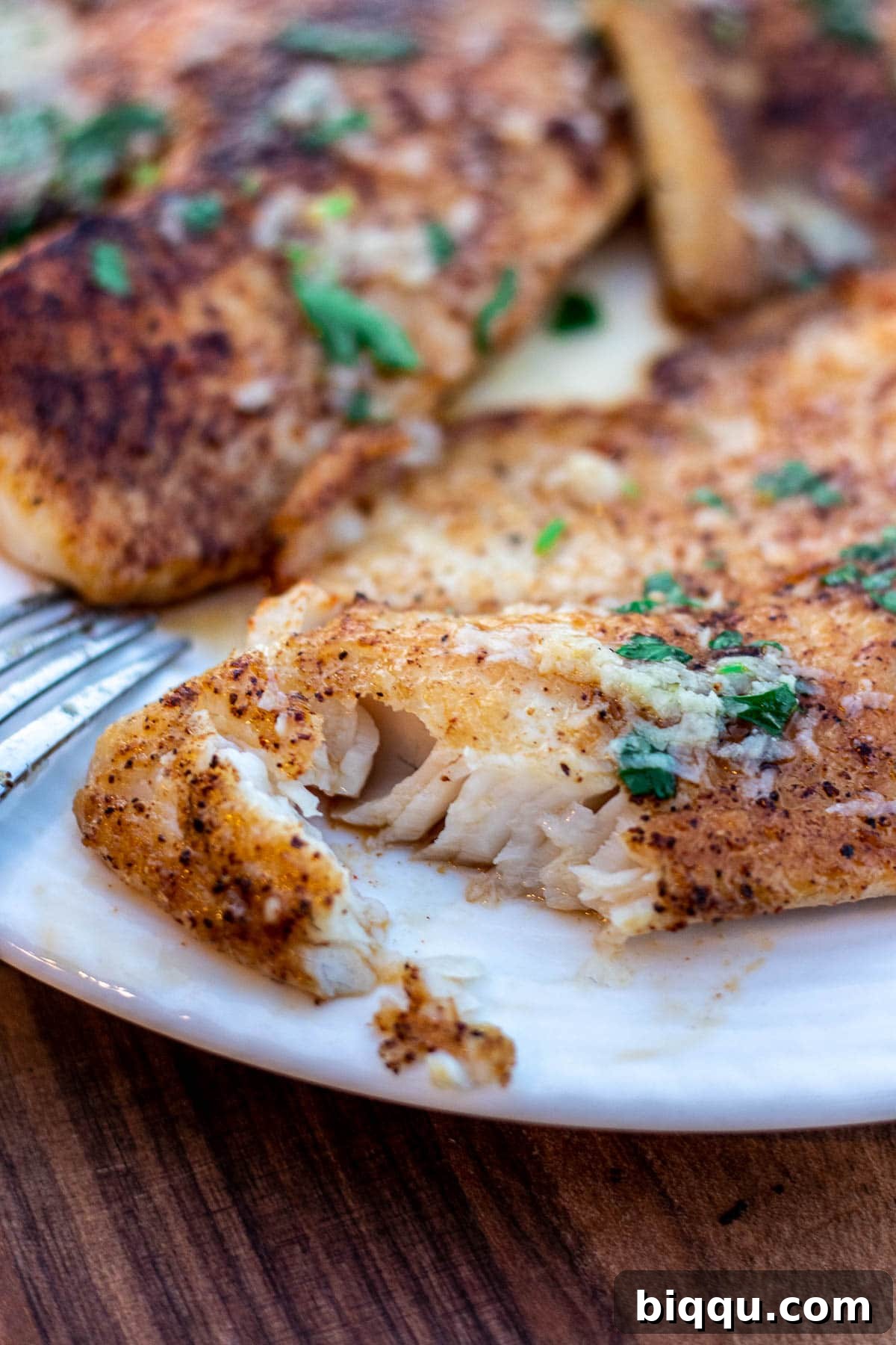 Close-up of flaky lemon butter tilapia fish on a white plate, highlighting its tender texture.
