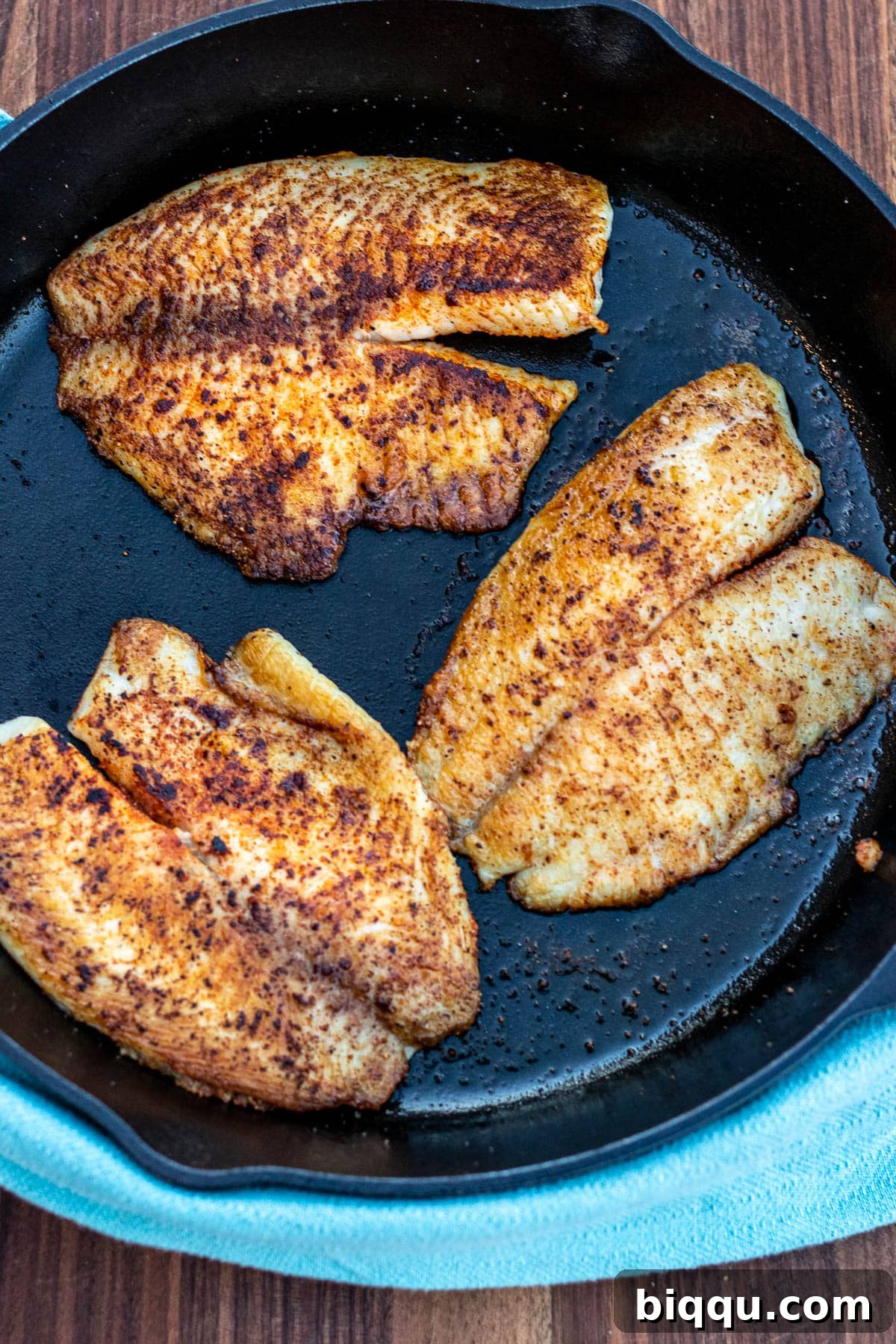 Tilapia fillets cooking in a hot cast iron pan, showing a golden crust forming.