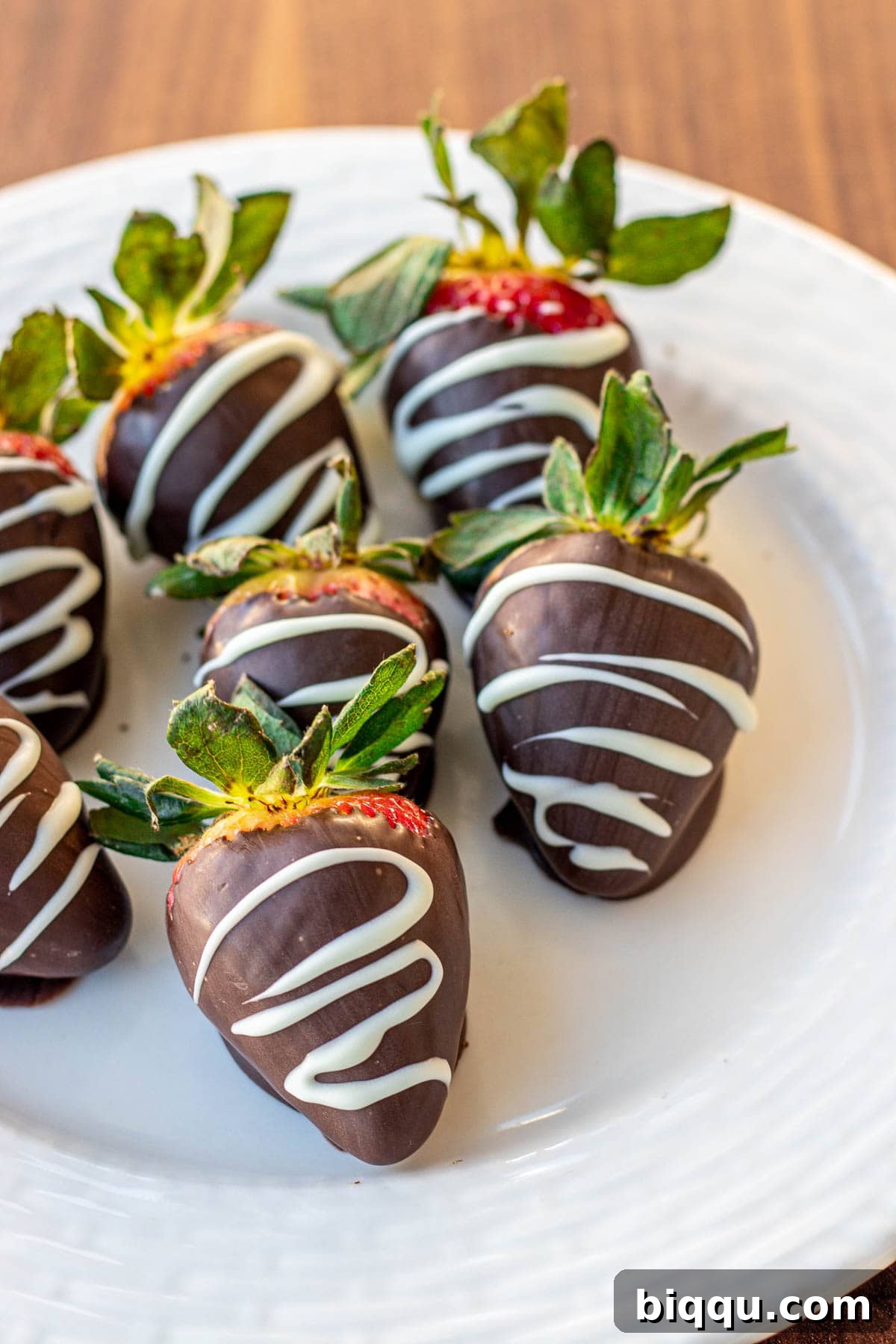 Beautifully arranged chocolate covered strawberries, elegantly drizzled with white chocolate for an added touch of sophistication, presented on a plate.