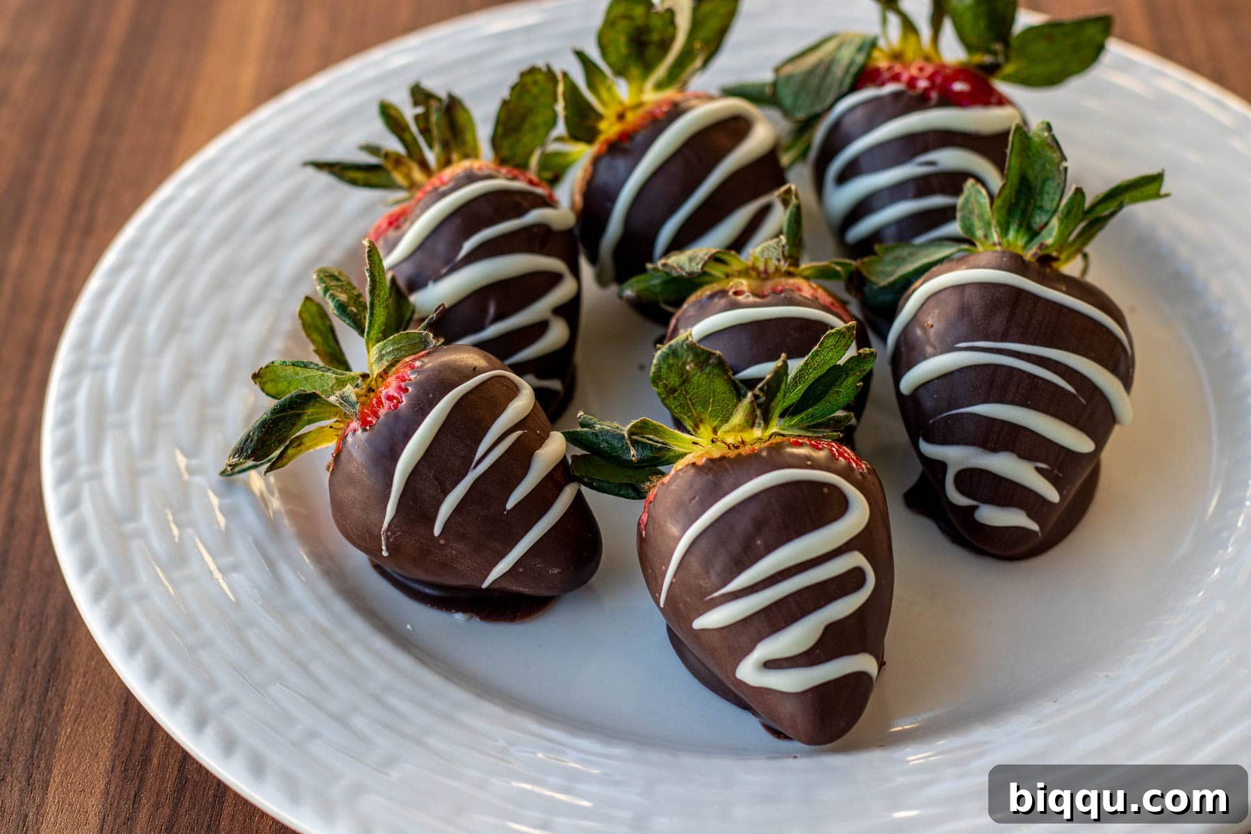 A stunning landscape shot of a plate piled high with glistening chocolate covered strawberries, showcasing their delicious appeal.