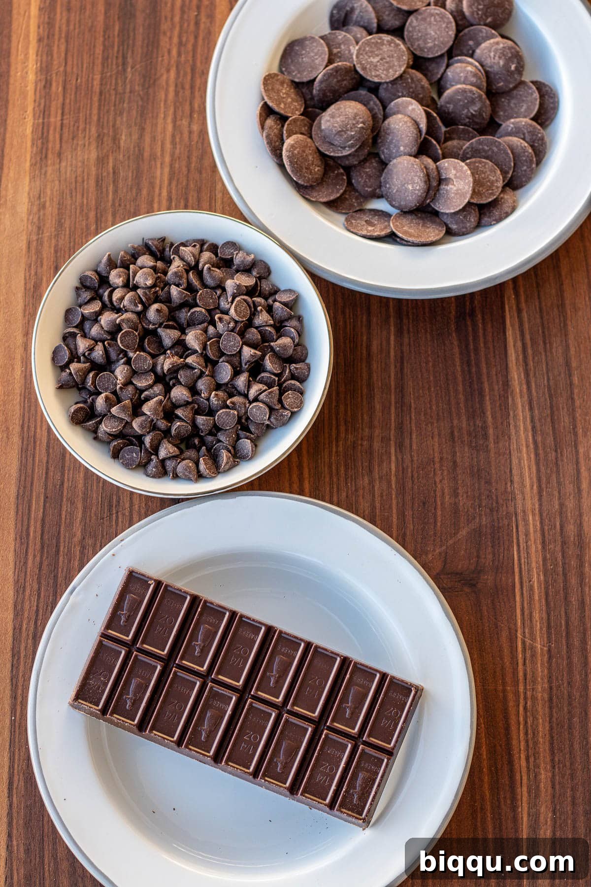 An assortment of different kinds of chocolate, including melting wafers, chocolate chips, and baking bars, laid out for a chocolate covered strawberry project.