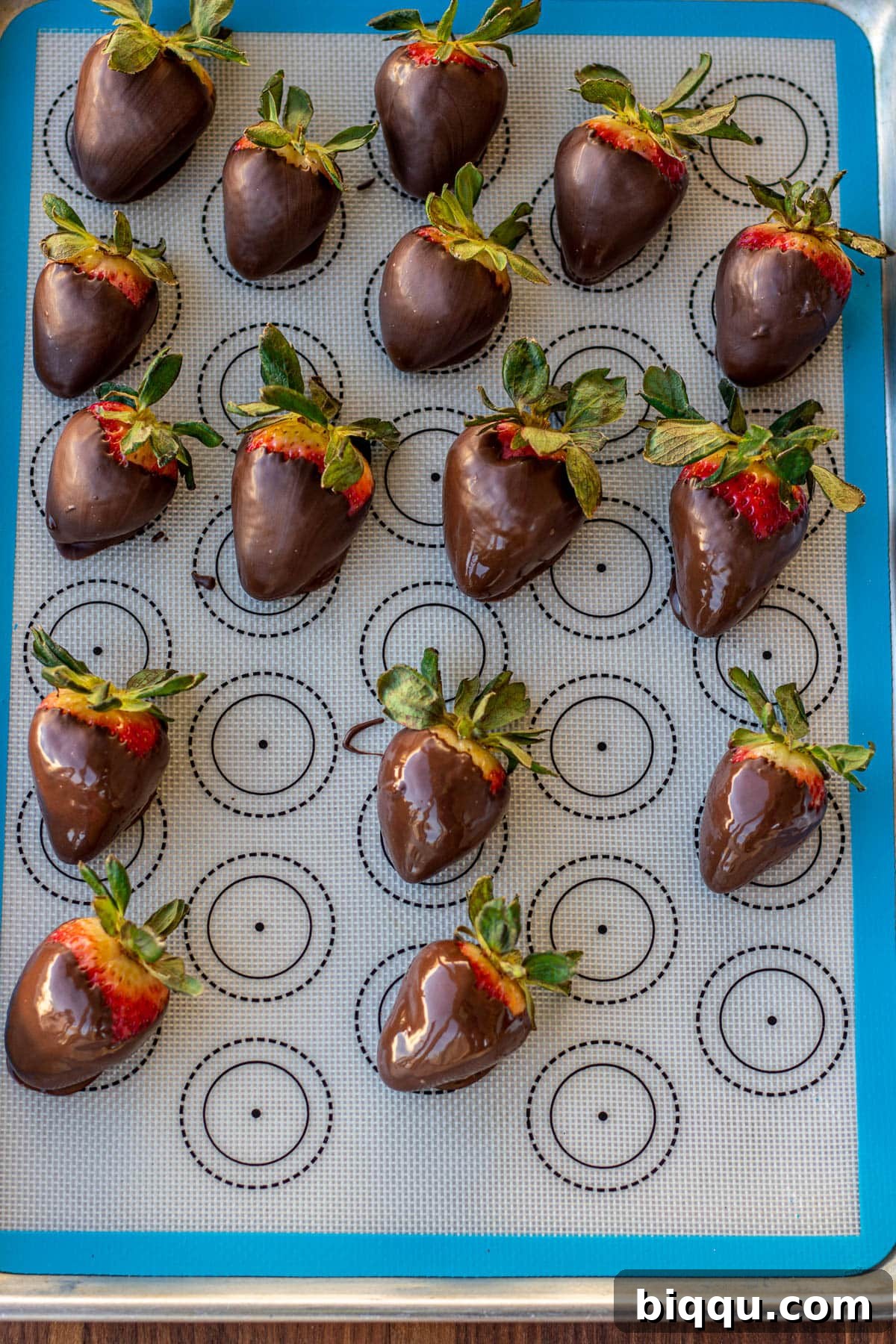 Rows of freshly made chocolate covered strawberries resting on a silicone mat, allowing the chocolate to set and harden.