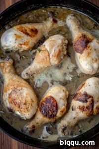 Chicken in a creamy mushroom sauce simmering in a cast iron skillet, with herbs.