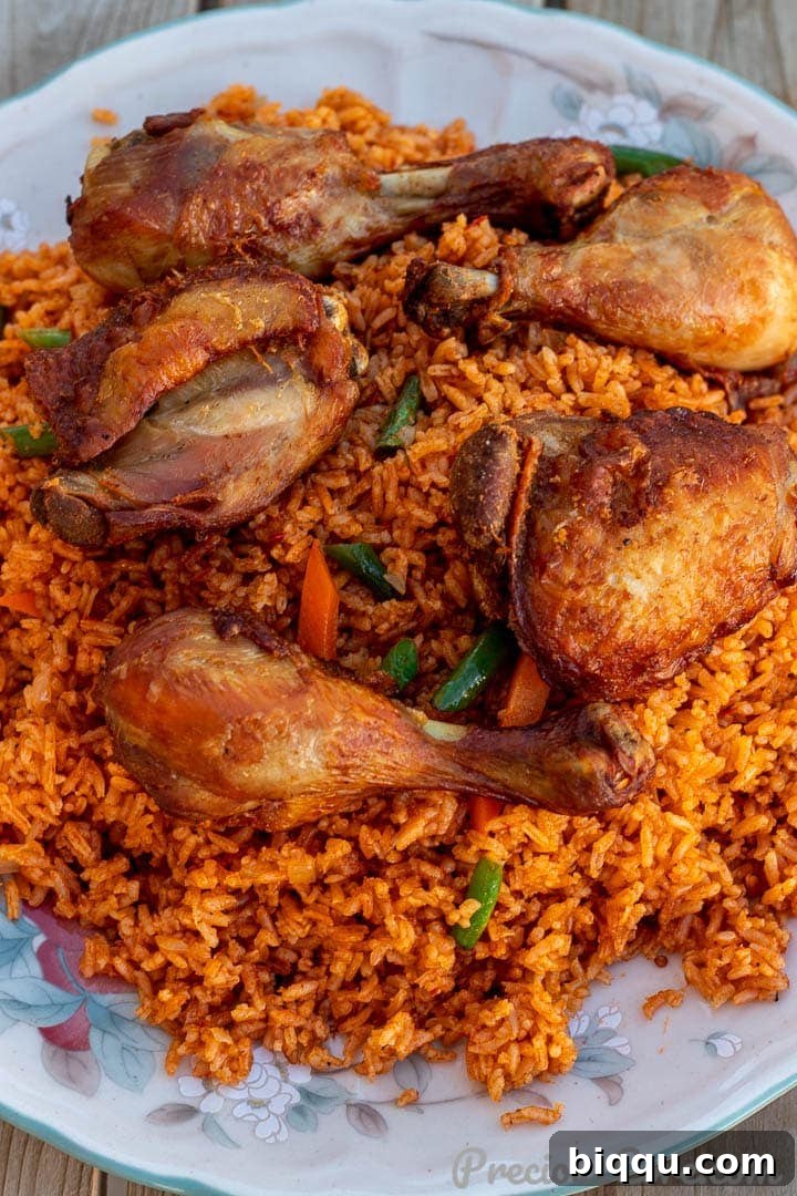 Jollof Rice on a serving platter with cooked chicken thighs and drumsticks on top, a classic West African dinner.