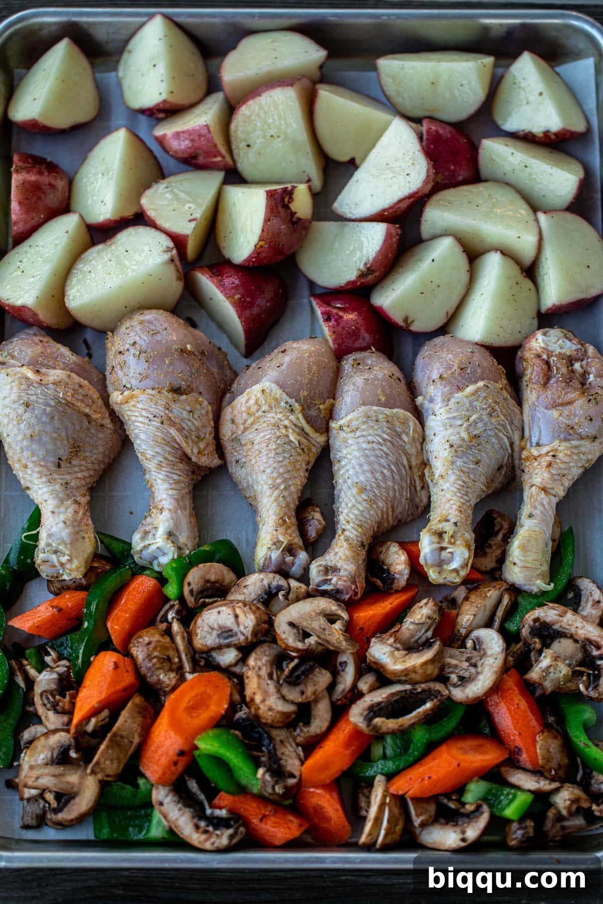 Baking sheet lined with seasoned potatoes, chicken, and mixed vegetables before cooking