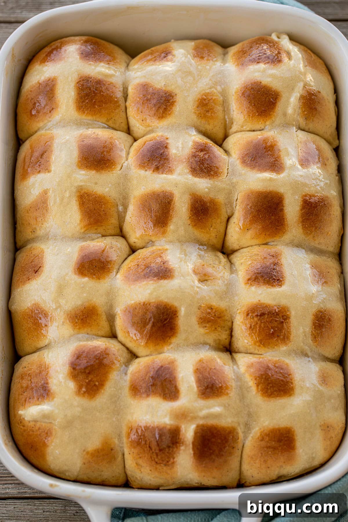 A large baking tray filled with numerous freshly baked Easter Hot Cross Buns, ready to be glazed.