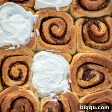 Cinnamon rolls in a pan, some of the rolls frosted with cream cheese frosting