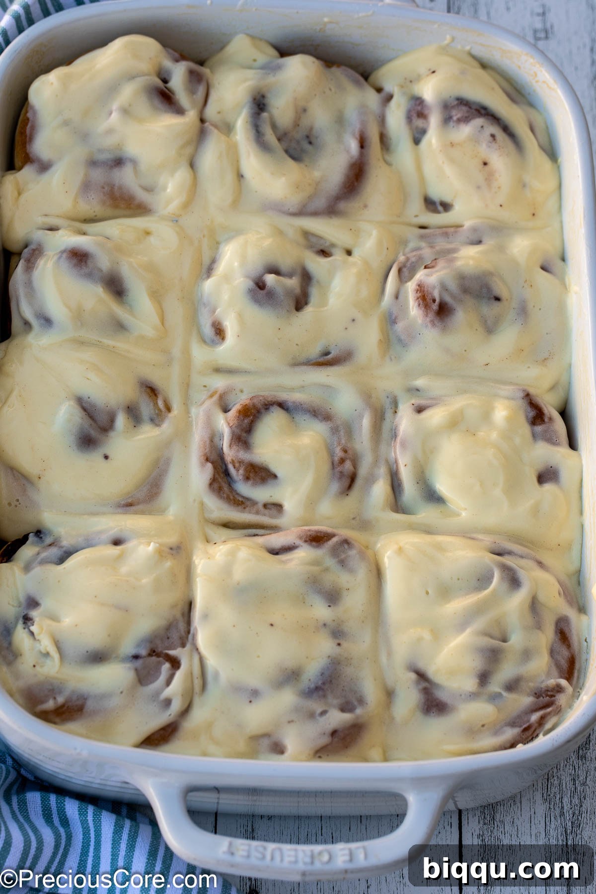 Cinnamon Rolls completely covered with cream cheese frosting in a white baking dish.